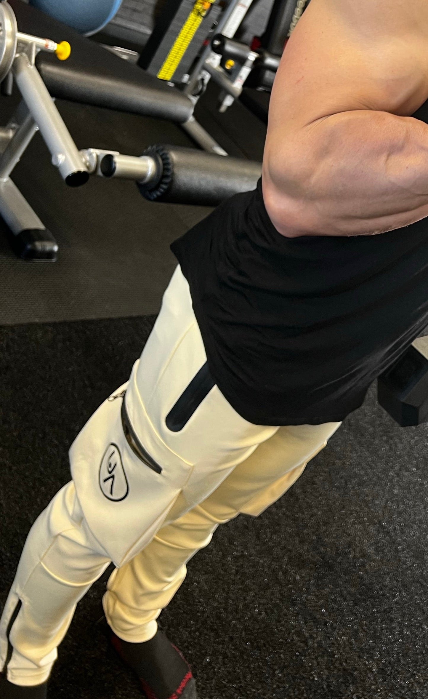 Man curling dumb bells in the gym, showing Sail joggers fro the side with logo and zipper side pockets.