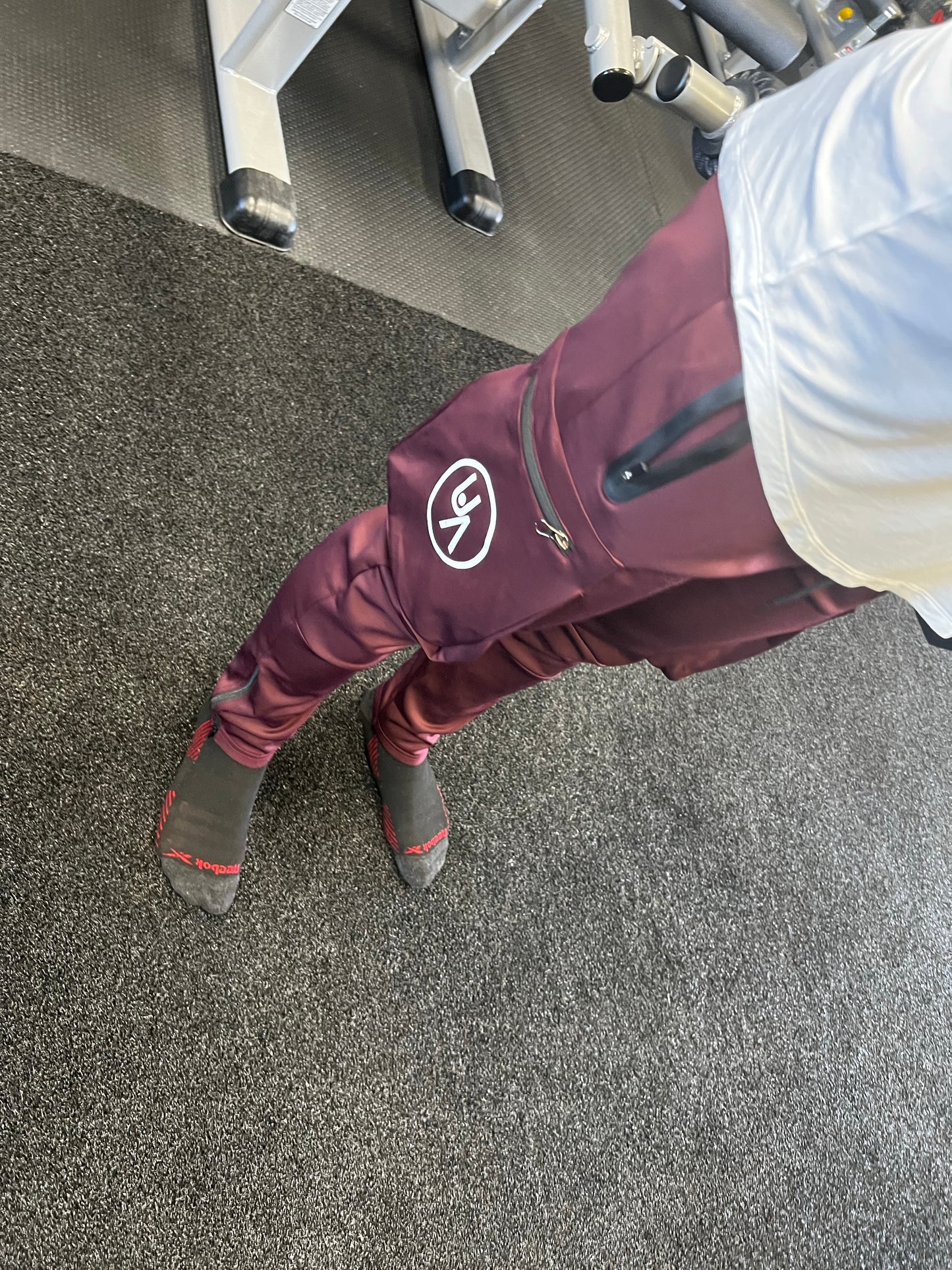 Man standing in gym wearing maroon warrior joggers. Side logo and zipper pockets showing.