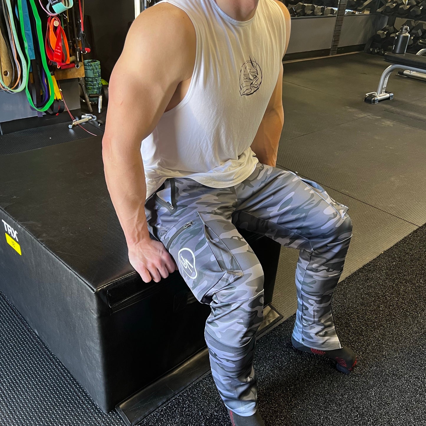 Man sitting in midnight camo Warrior joggers. Side logo and zipper pockets