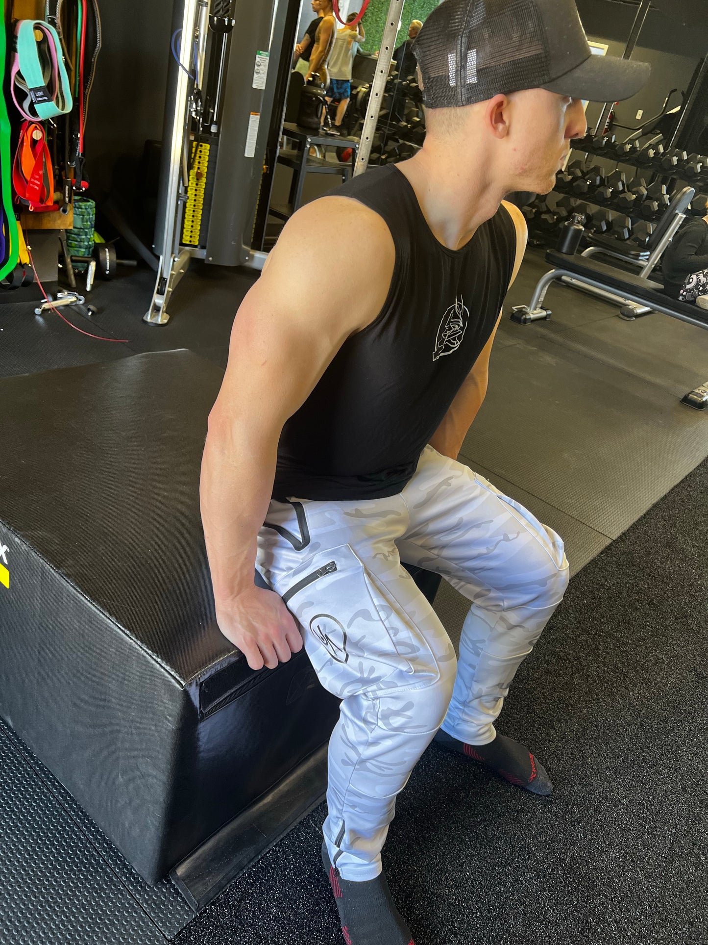 Man sitting in white camo warrior joggers.  Zipper ankle, side pocket and logo showing.